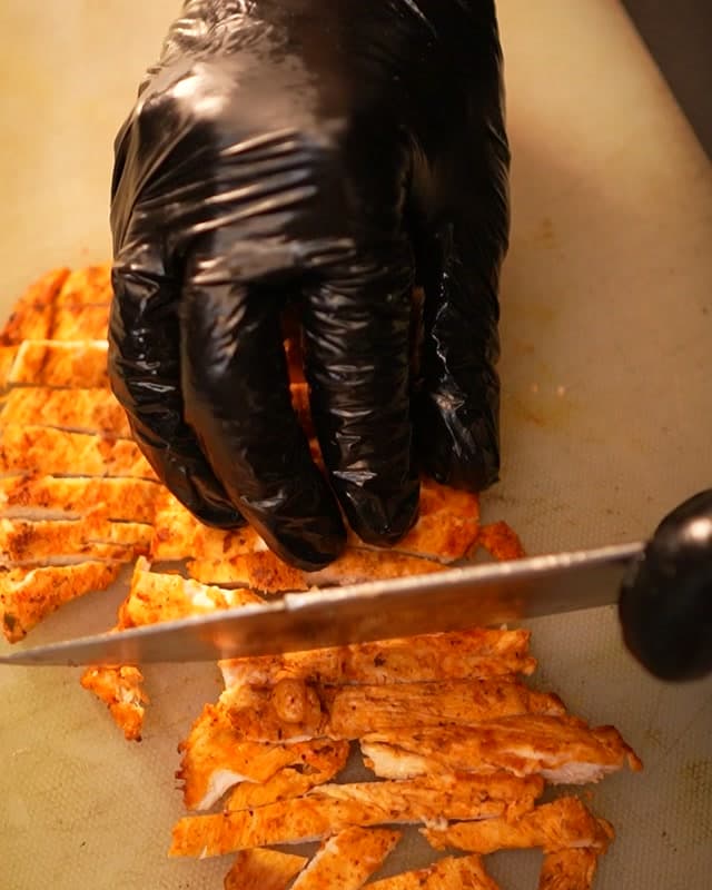 Grilled chicken sliced on the board in the Sufraq kitchen, the griddle still lit behind it